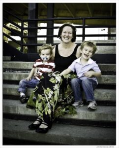 A smiling woman and two young boys sitting on concrete steps in an urban area.